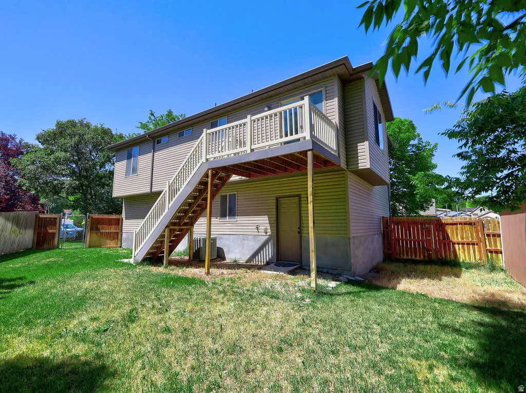 Rear exterior featuring a spacious wooden deck with railings, an exterior staircase, and tan siding