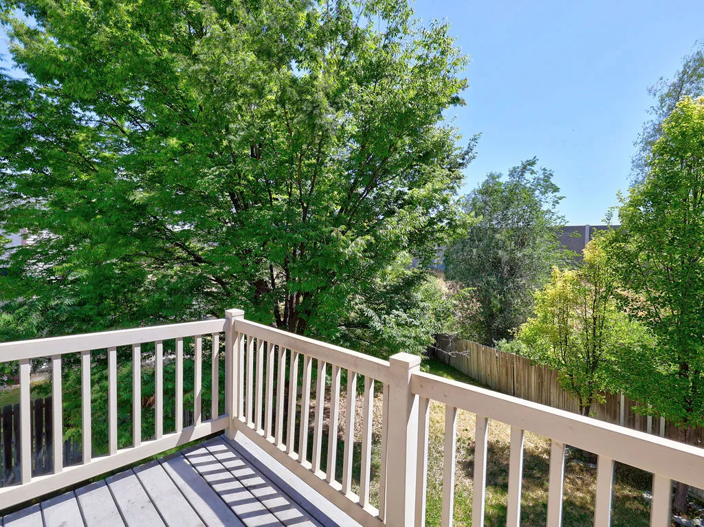 Outdoor deck with composite decking and light-colored railing, surrounded by mature trees and natural landscaping