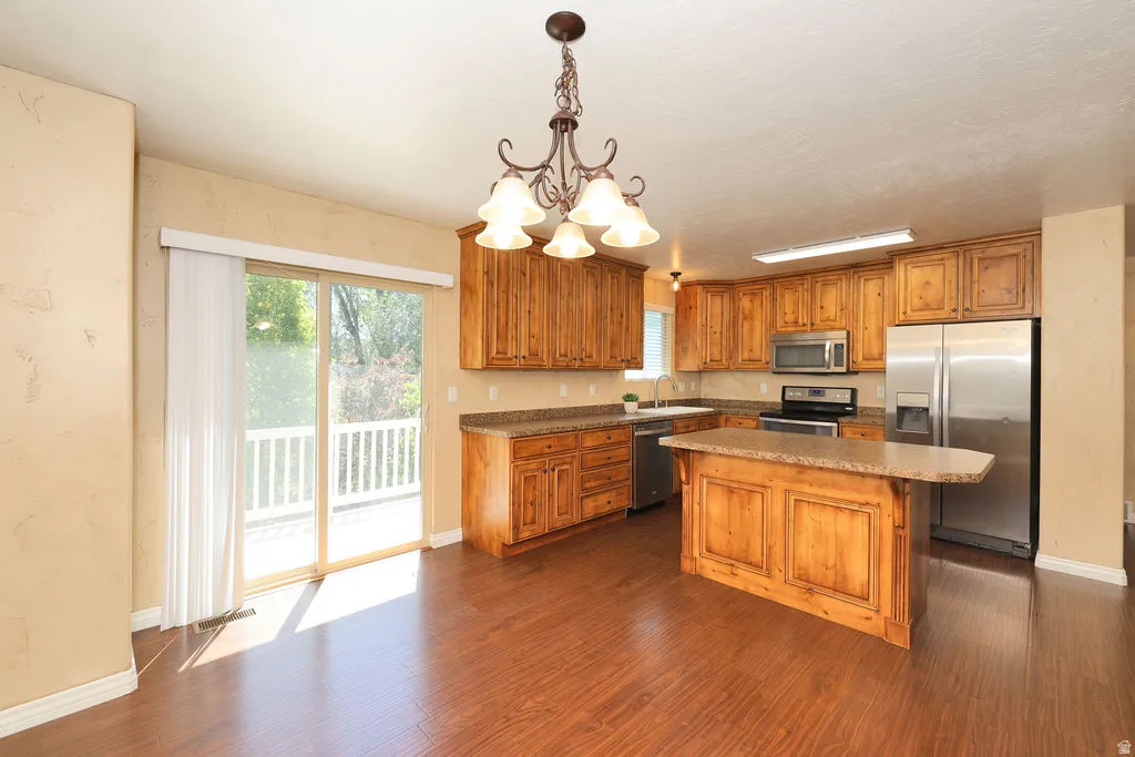 Kitchen featuring wood-finish flooring, natural wood cabinetry, a central island with an extended countertop, stainless steel appliances, and a sliding glass door opening to an outdoor deck