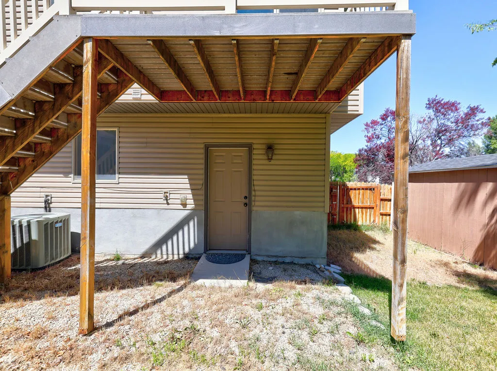 Exterior featuring light-toned vinyl siding, a ground-level access door, and an upper-level deck with wooden supports