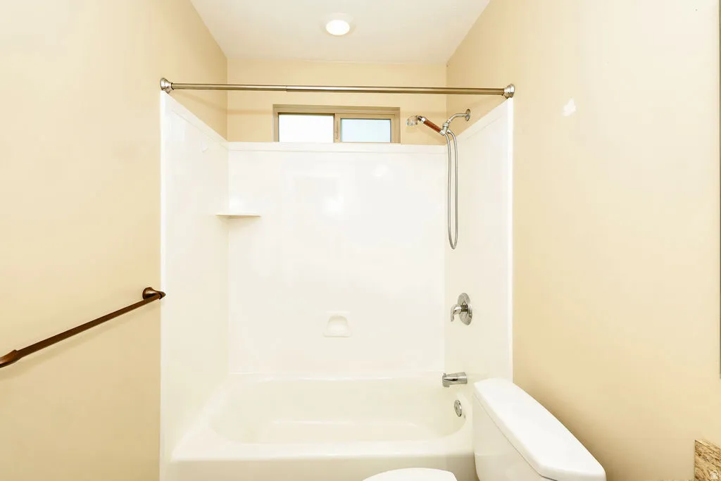 Bathtub and shower combination featuring a white composite surround, chrome fixtures, and an overhead window