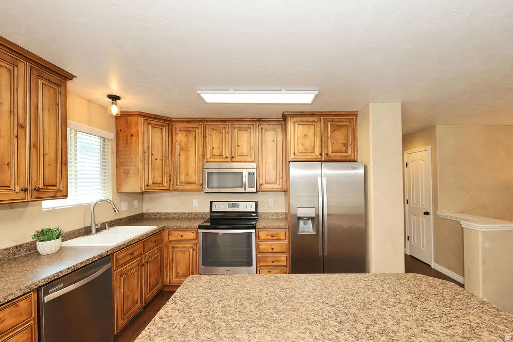 Kitchen featuring wood cabinetry, stainless steel appliances, a double basin sink with a gooseneck faucet, and speckled countertops