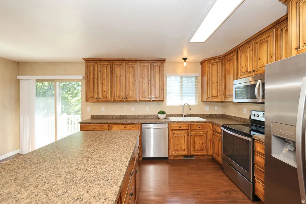 Kitchen featuring wood-finish cabinetry, stainless steel appliances, speckled countertops, and wood-finish flooring