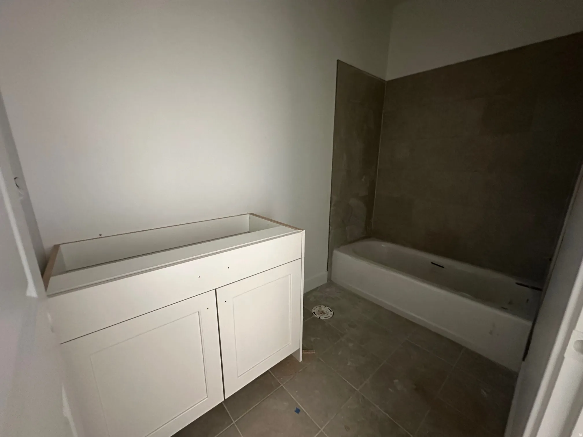 White vanity base with Shaker-style cabinet doors, a drop-in bathtub, and dark grey tile shower surround