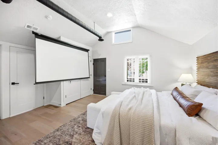 Vaulted ceiling room featuring light wood-finish flooring and a large, retractable projection screen