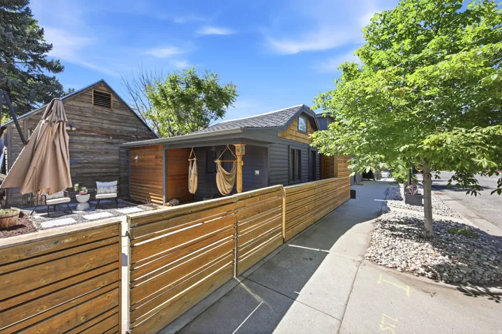 Wood-slat fencing enclosing a side yard with a patio featuring concrete pavers, a privacy wall with wood siding, and a covered porch area
