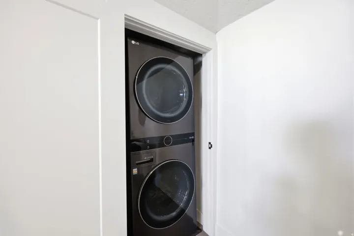 Integrated dark-finish stacked washer and dryer unit within a dedicated alcove, featuring a white painted door frame and clean white walls