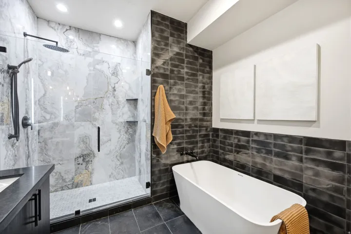 Contemporary bathroom featuring a freestanding tub, glass-enclosed shower with large format tile, and dark subway tile accent wall