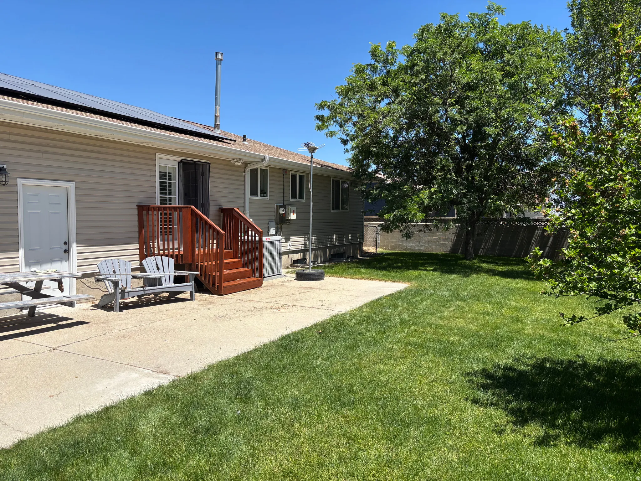 Spacious backyard featuring a concrete patio, wood deck with stairs, a large mature tree, and a grassy expanse