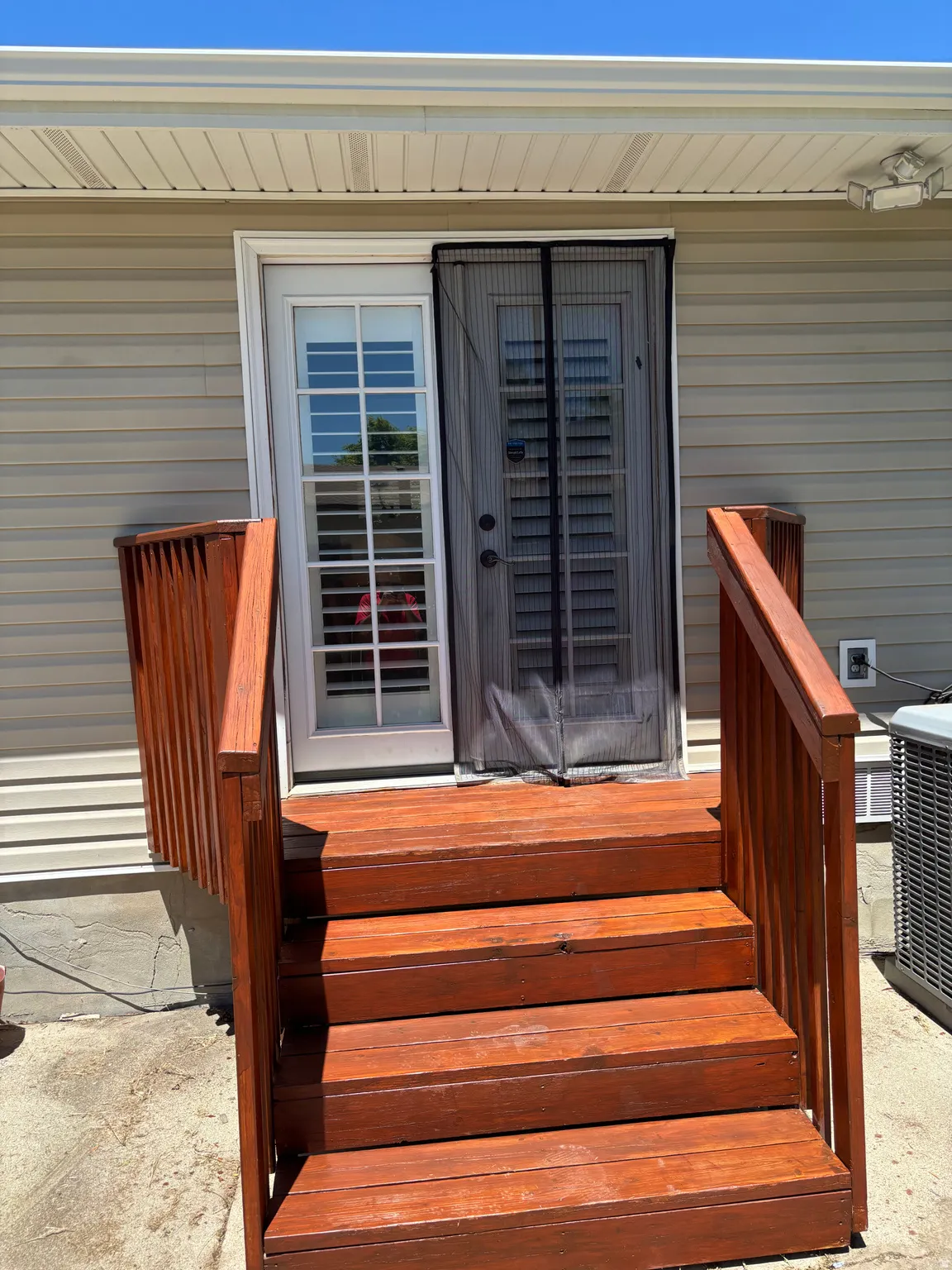 Exterior rear entry featuring a multi-pane glass door with interior shutters, a separate screen door, and a rich wood-finish deck with handrails