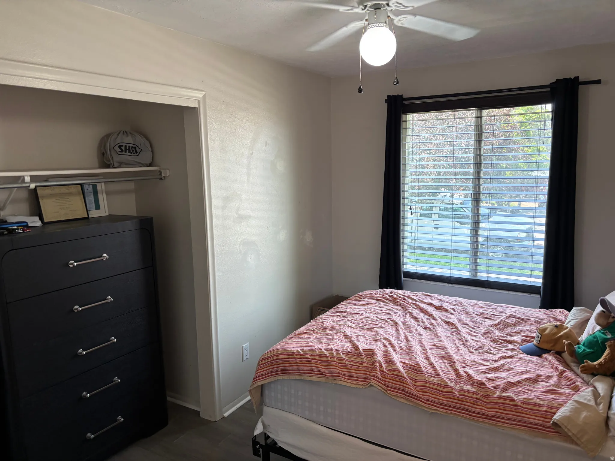 Interior room featuring a ceiling fan with integrated lighting, a window with horizontal blinds, and a built-in closet with a shelf and hanging rod