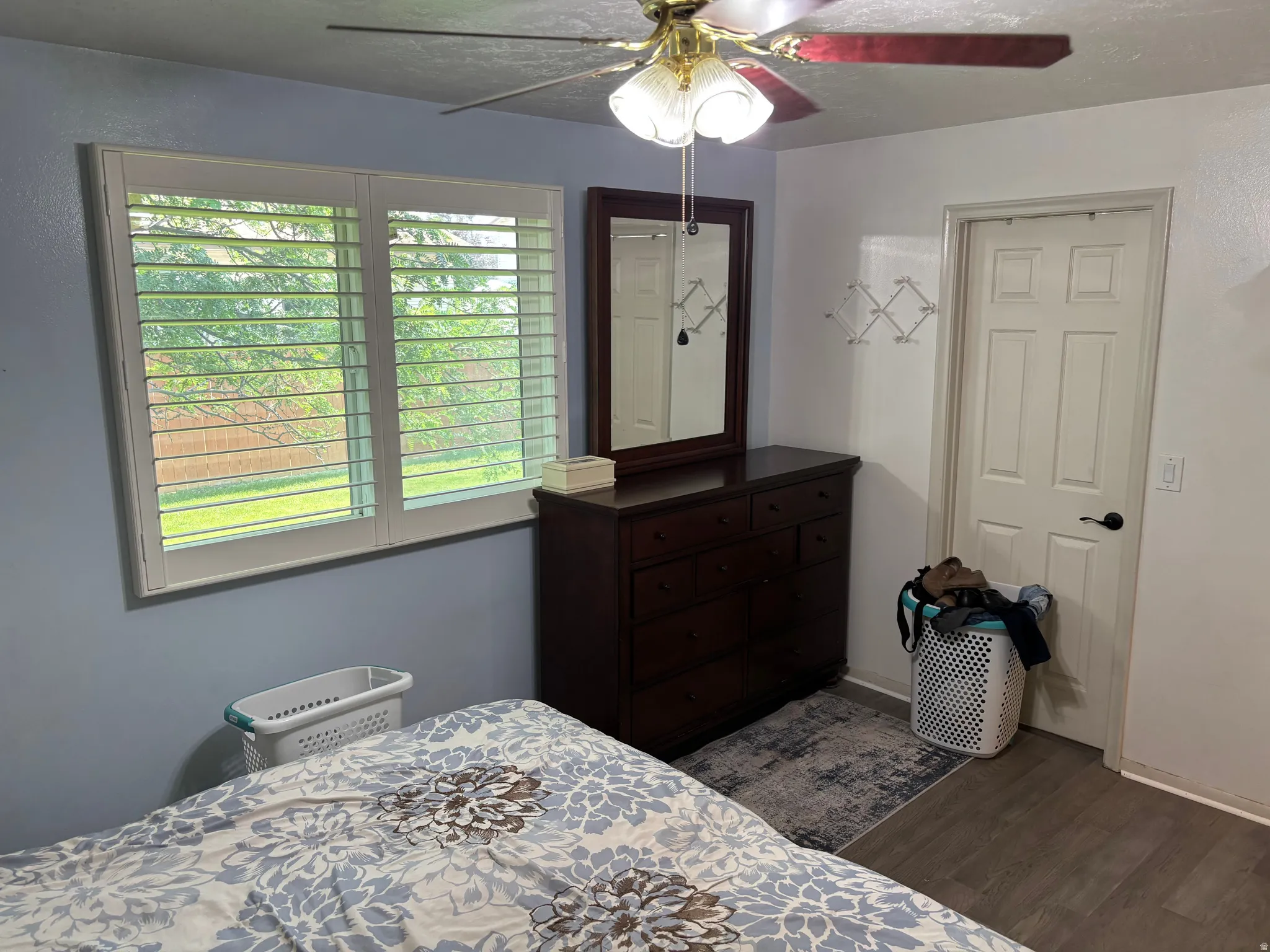 Room featuring a window with white louvered shutters, wood-finish flooring, and a ceiling fan with light fixture