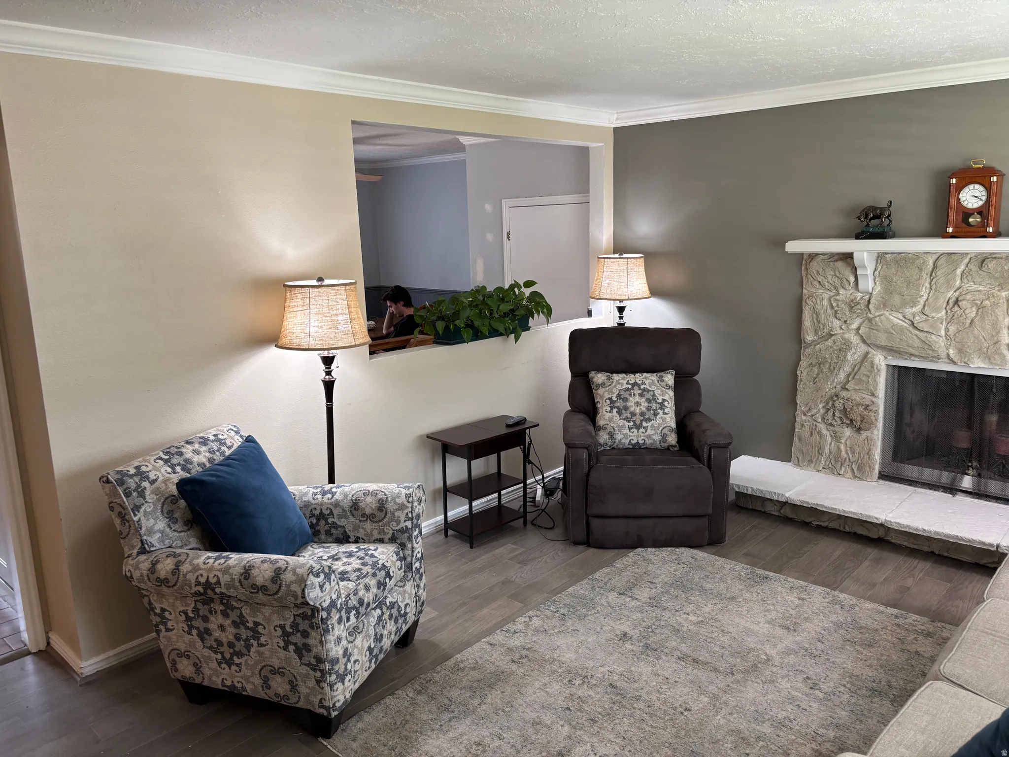 Living area featuring a stone-clad fireplace with hearth, wood-finish flooring, and crown molding