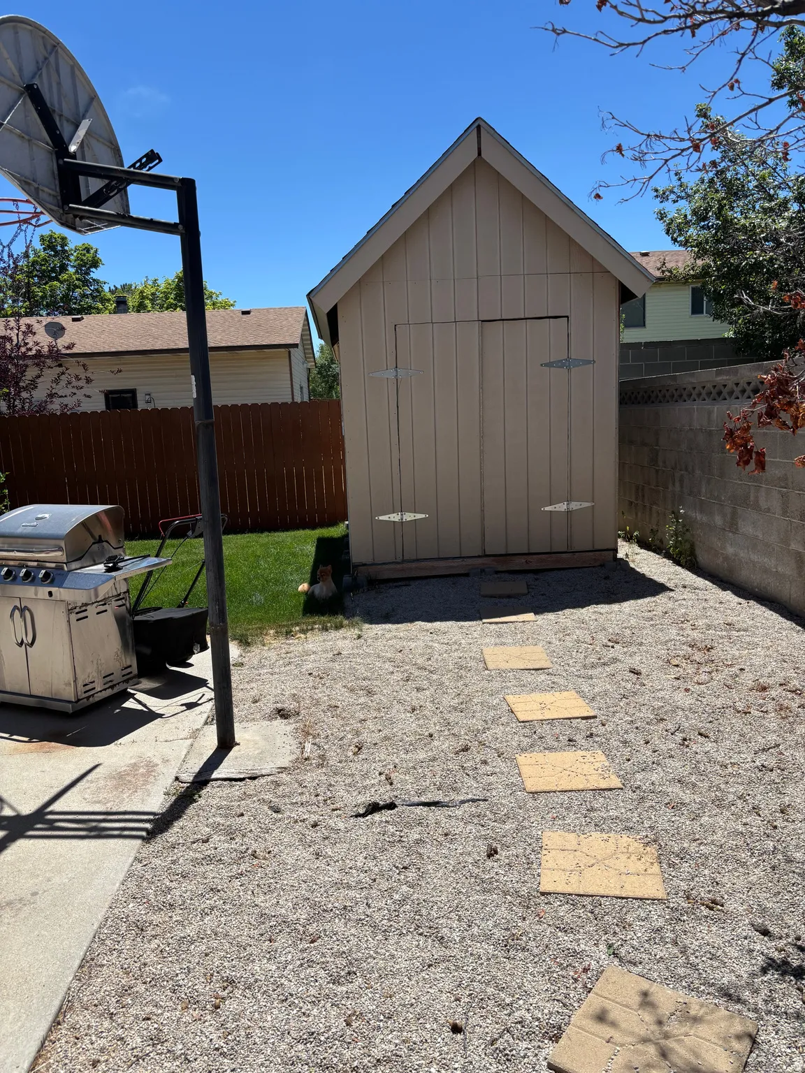 Gable-roof storage shed with double doors, set on a gravel-covered yard with a concrete block wall and wood fence perimeter