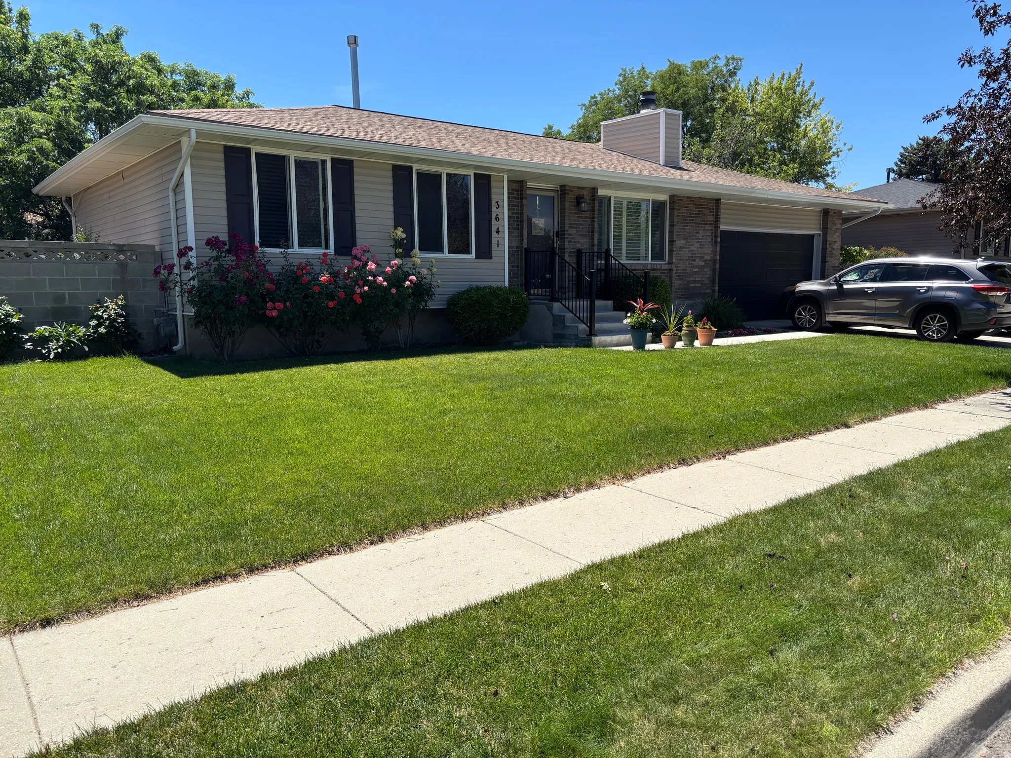 Ranch-style exterior featuring a combination of brick and siding, a front entry with handrails, an attached garage, a paved driveway, and mature landscaping with flowering shrubs