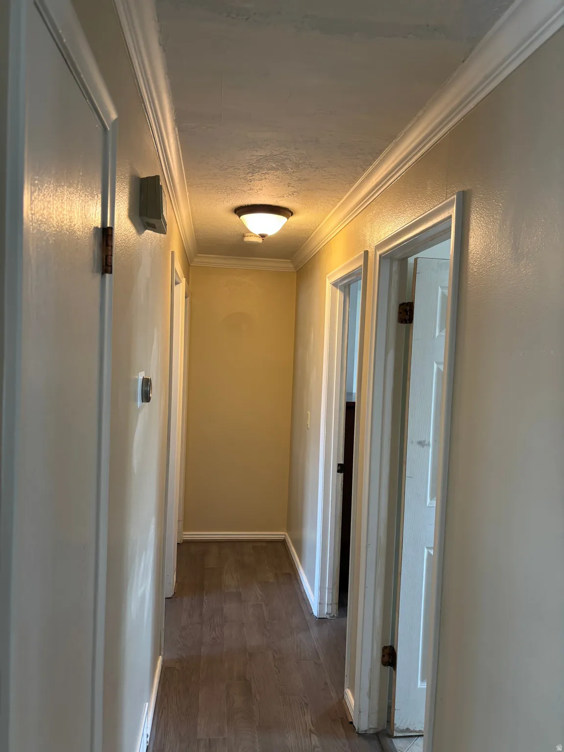 Hallway featuring wood-finish flooring, white baseboards, white crown molding, and recessed lighting