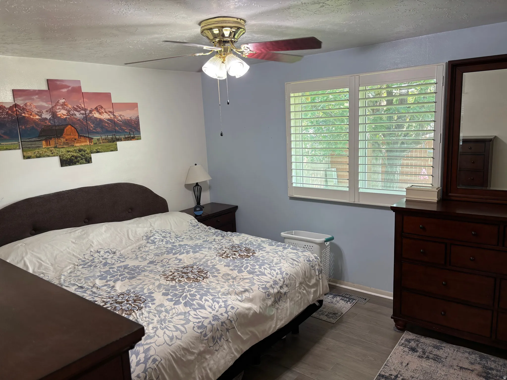 Bedroom featuring a ceiling fan with integrated lighting, wood-finish flooring, and white window shutters