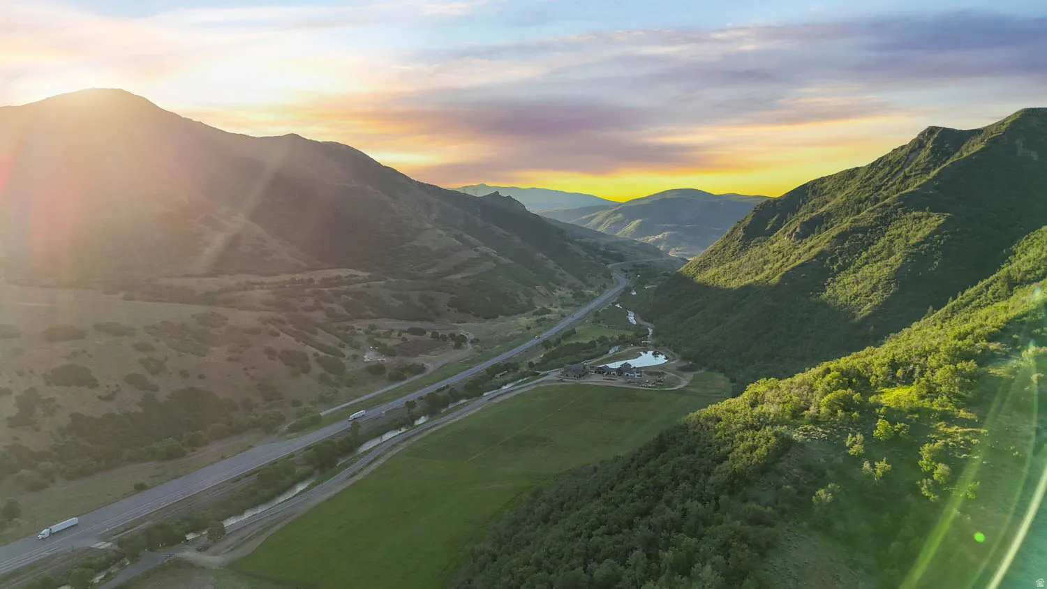 Expansive mountainous landscape featuring a valley with a highway, a river, and significant green space