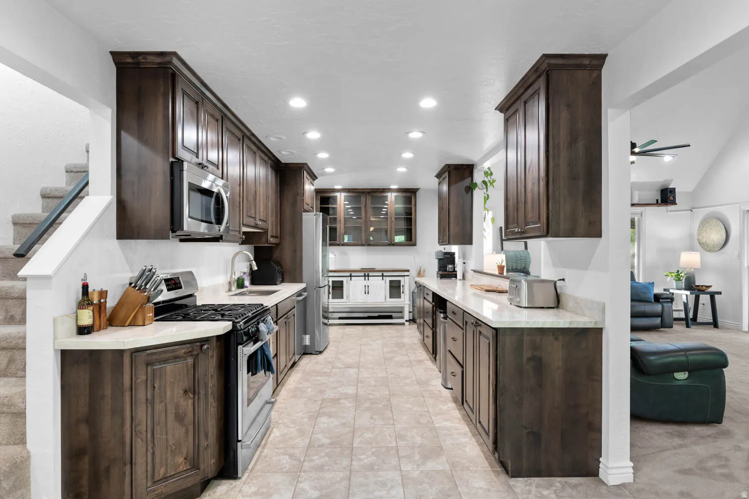 Galley kitchen featuring dark wood cabinetry, stainless steel appliances, and light-toned countertops