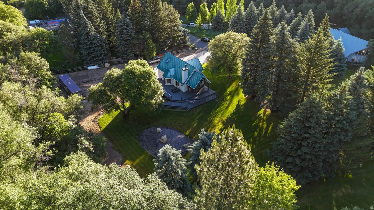 Expansive property featuring a multi-story residence with a green roof, surrounded by mature evergreen and deciduous trees