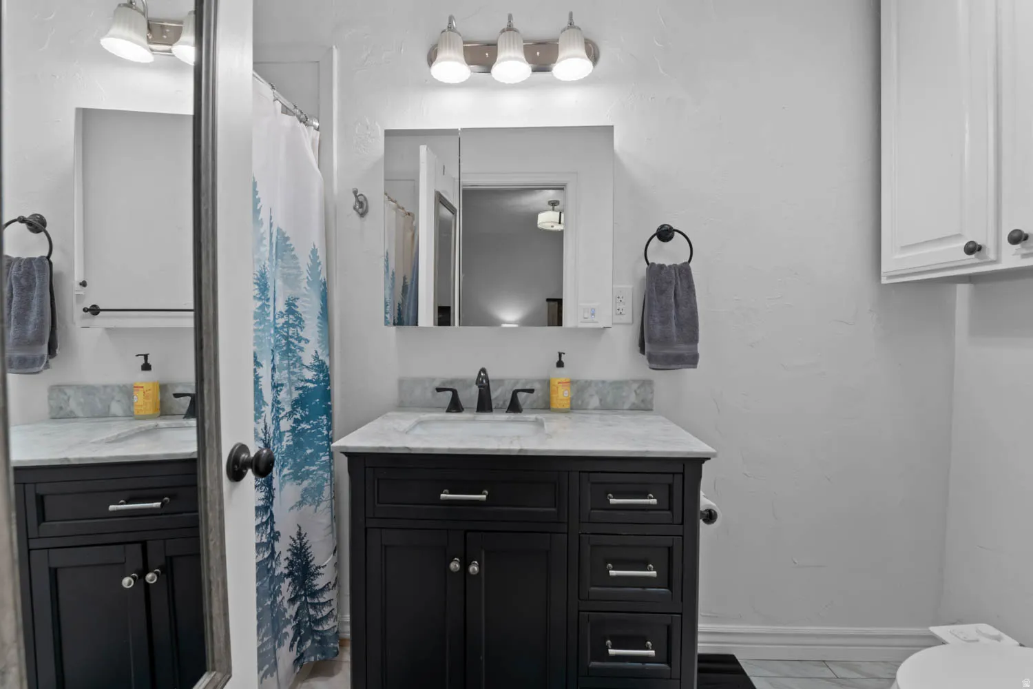Bathroom vanity featuring a black cabinet with silver hardware, a light-toned countertop, and a recessed medicine cabinet with integrated lighting