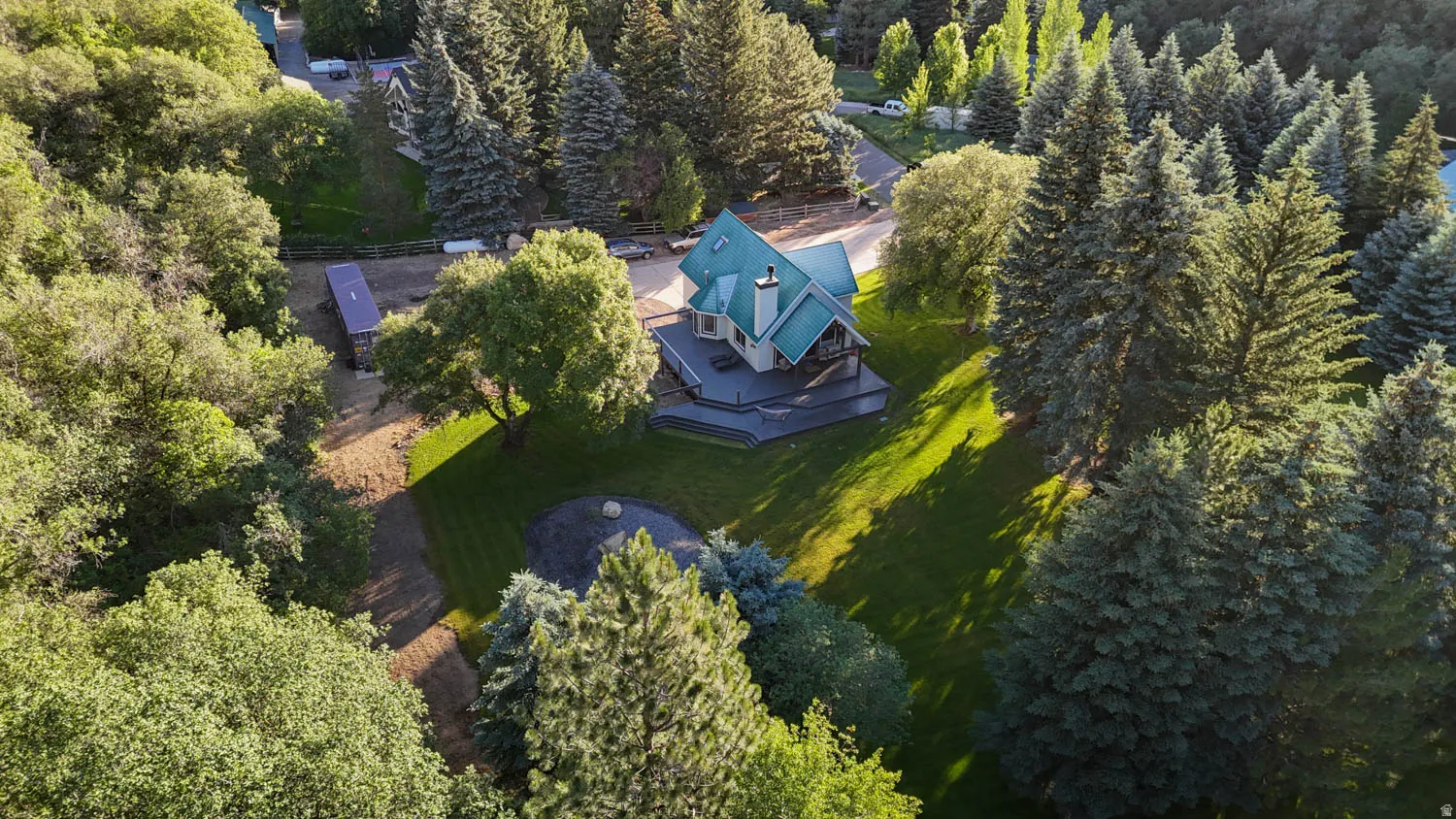 Multi-level residence with a distinct teal roof, surrounded by mature evergreen and deciduous trees