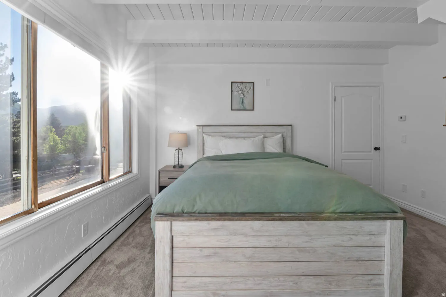 Bedroom featuring a large multi-pane window, white textured walls, and a beamed ceiling