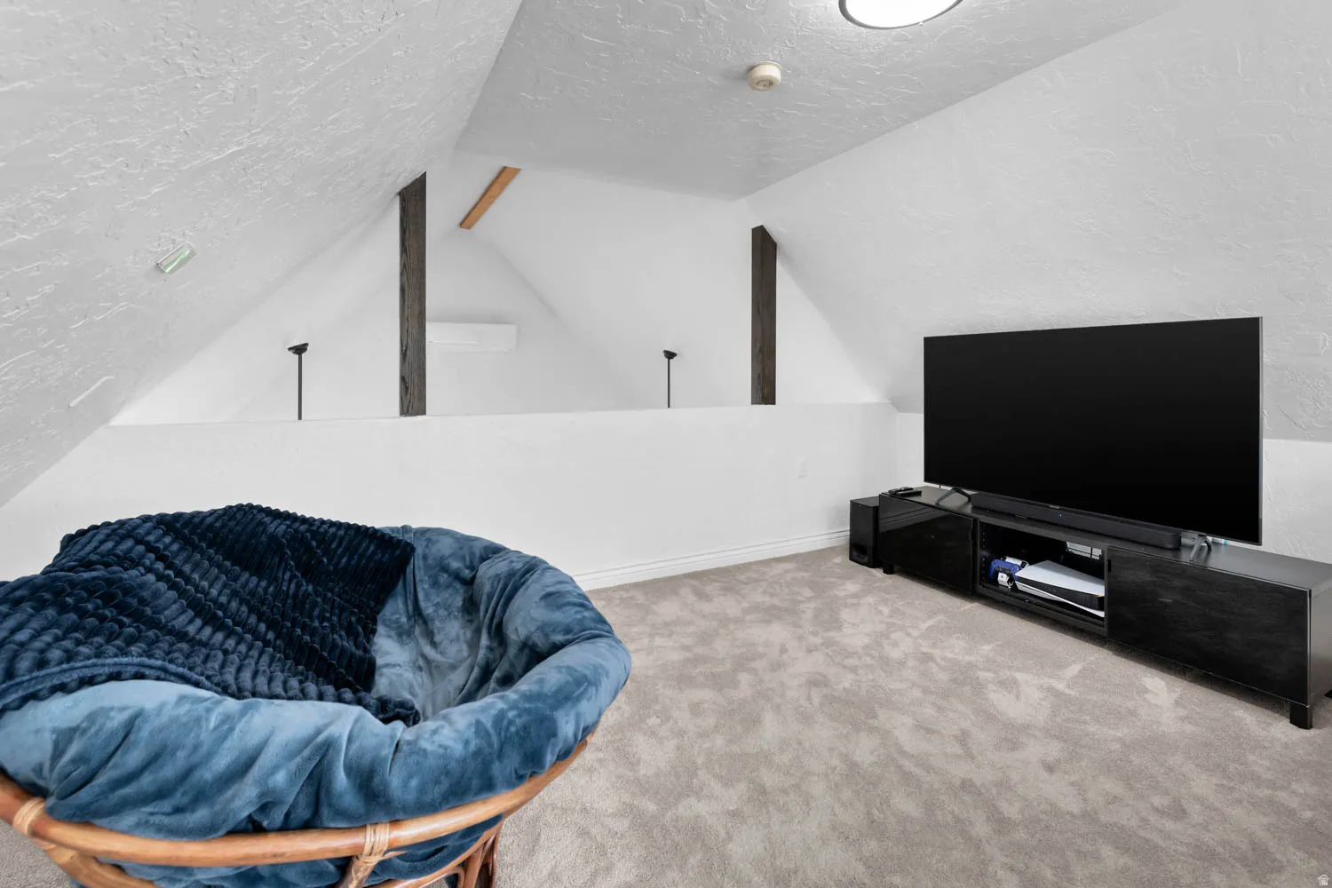 Attic space featuring sloped ceilings, exposed structural beams, and light gray carpeting