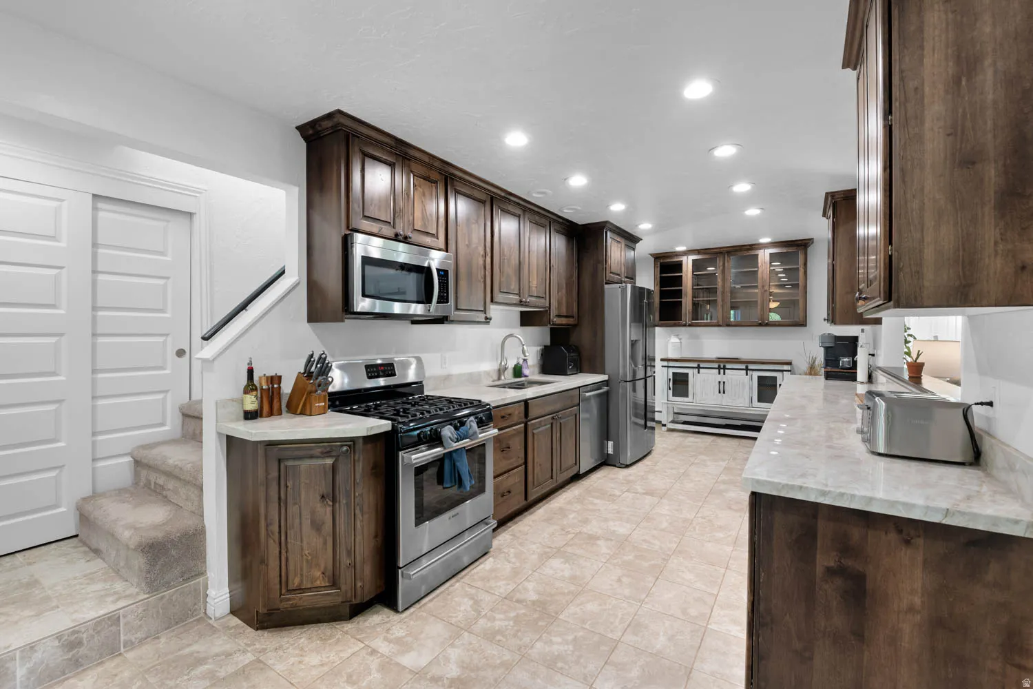 Kitchen featuring wood cabinetry, stainless steel appliances, light-colored countertops, tiled flooring, and recessed lighting