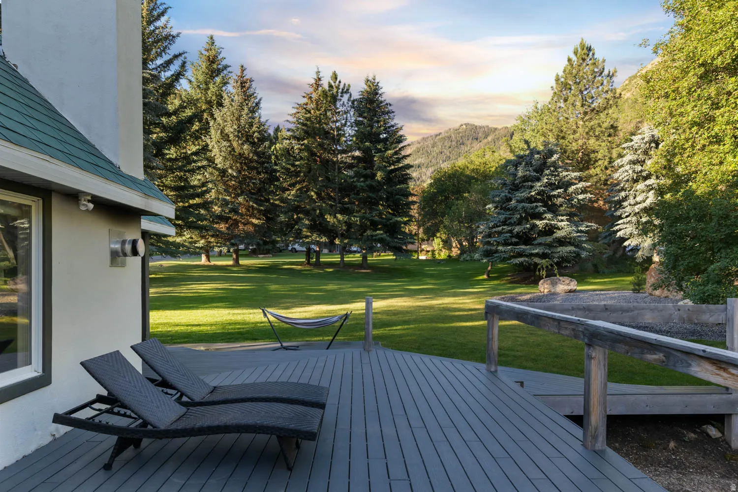 Spacious outdoor deck with composite decking and wood railing, overlooking a large grassy area with mature trees and mountain scenery