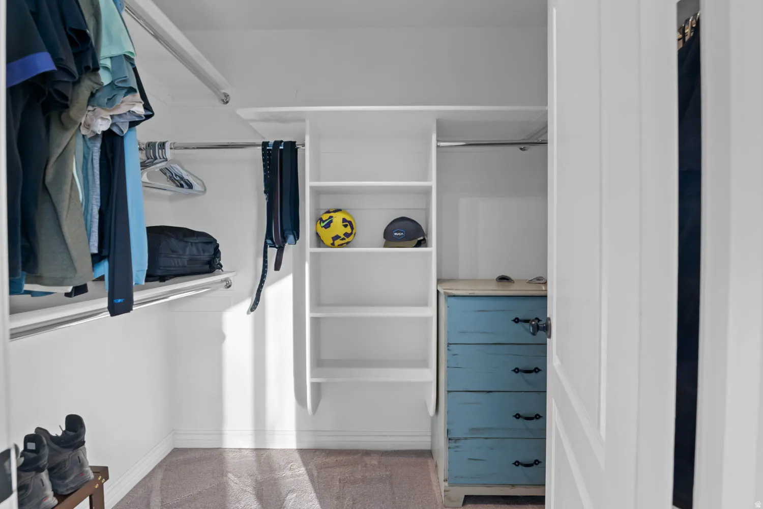 Walk-in closet featuring white built-in shelving, chrome hanging rods, and carpeting