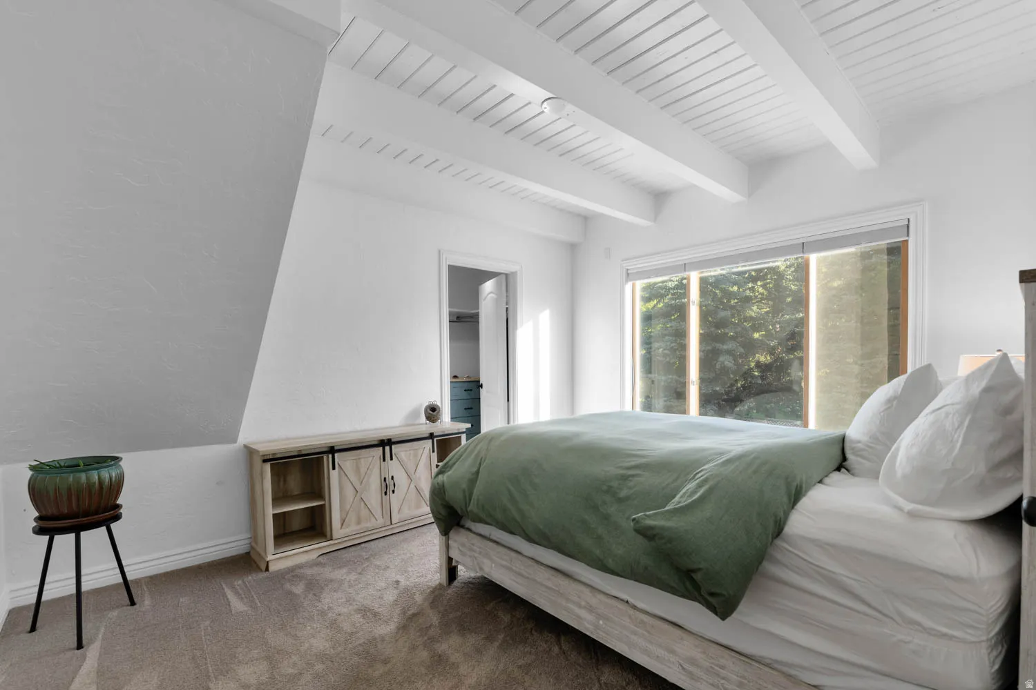 Spacious room featuring a vaulted ceiling with exposed white beams, recessed lighting, and a large window