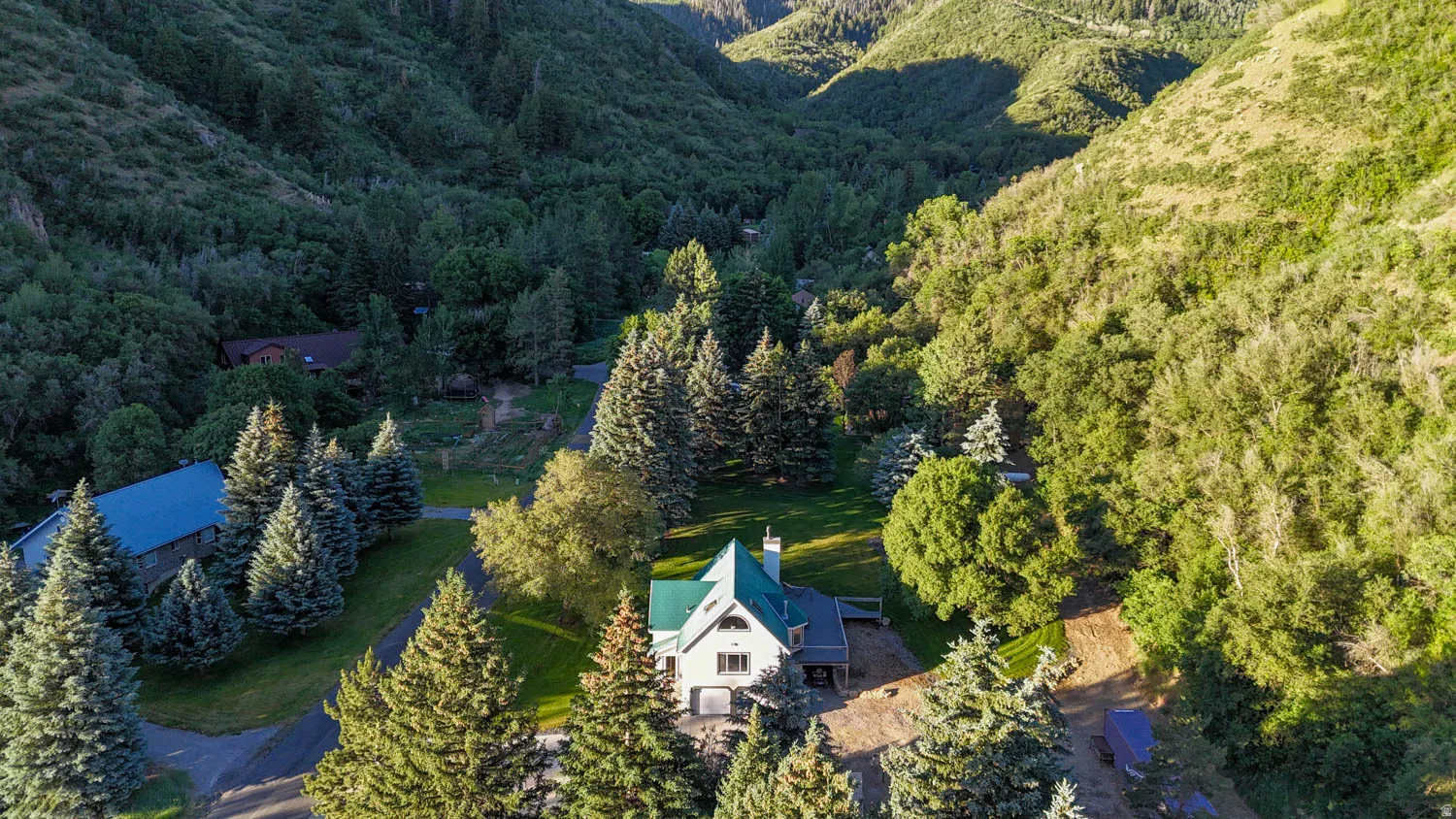 Mountainous terrain surrounding a property featuring a green-roofed residence, a paved driveway, and mature evergreen trees
