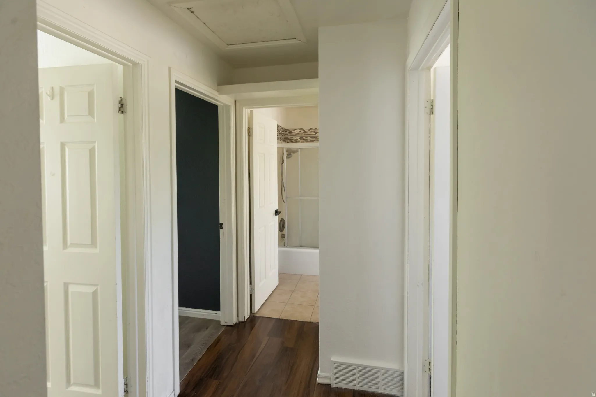 Hallway featuring wood-finish flooring, white paneled doors, and a tiled bathroom with a tub/shower combination