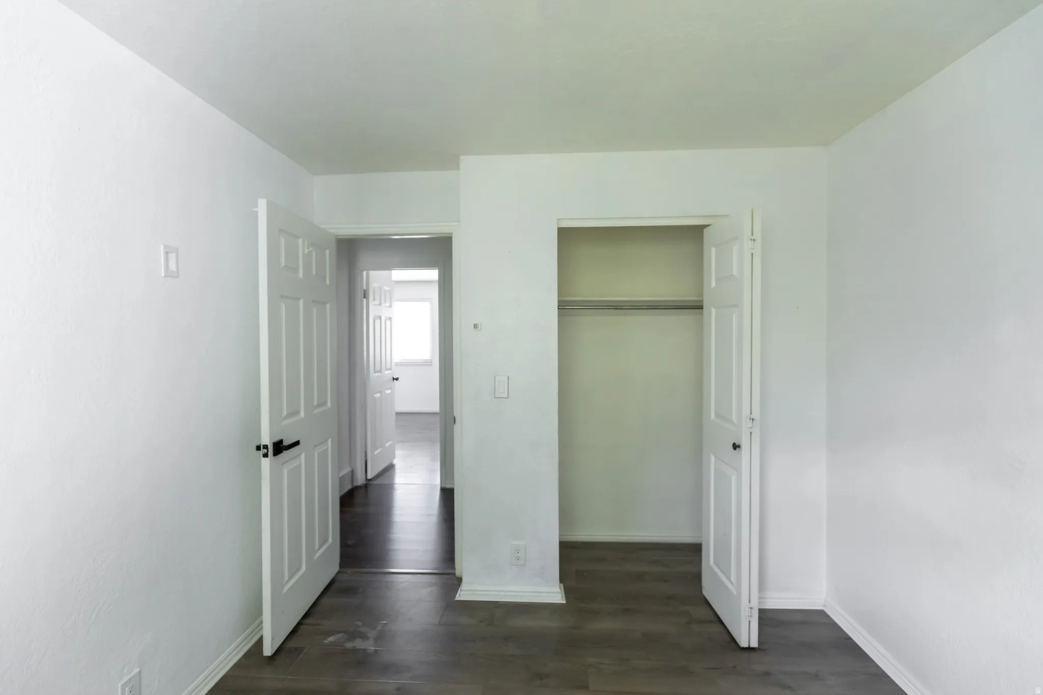 Bedroom featuring wood-finish flooring, a six-panel door with dark hardware, a built-in closet with hanging rod, and white baseboards