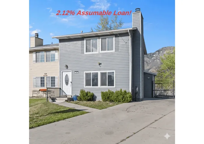 Gray-sided townhouse with a white oval-paneled entry door, concrete driveway, and a prominent chimney