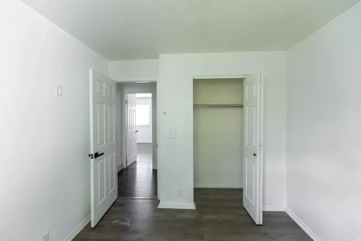 Bedroom featuring wood-finish flooring, a six-panel door with dark hardware, a built-in closet with hanging rod, and white baseboards