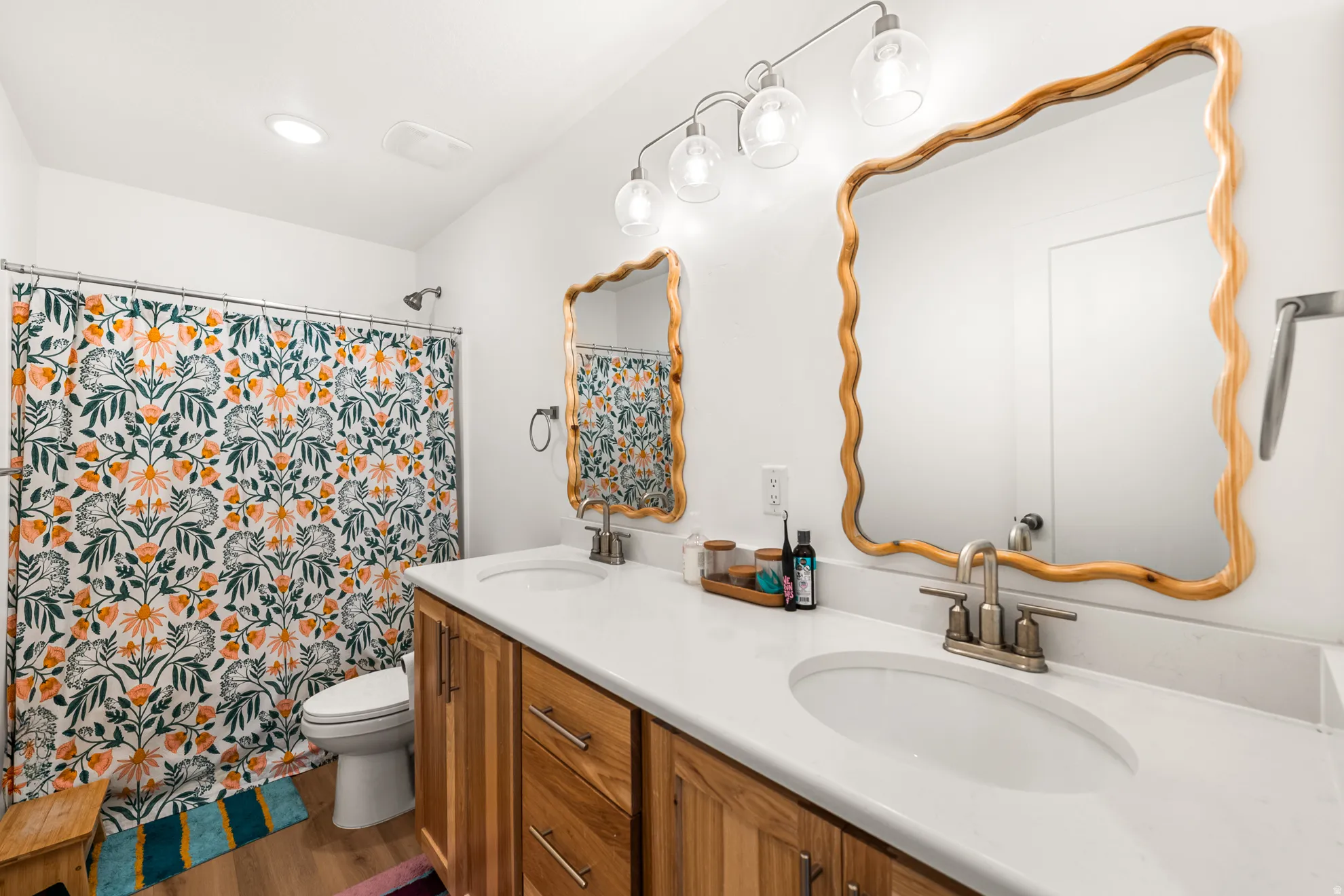 Dual vanity bathroom featuring wood-finish cabinetry, white countertops, and contemporary light fixtures