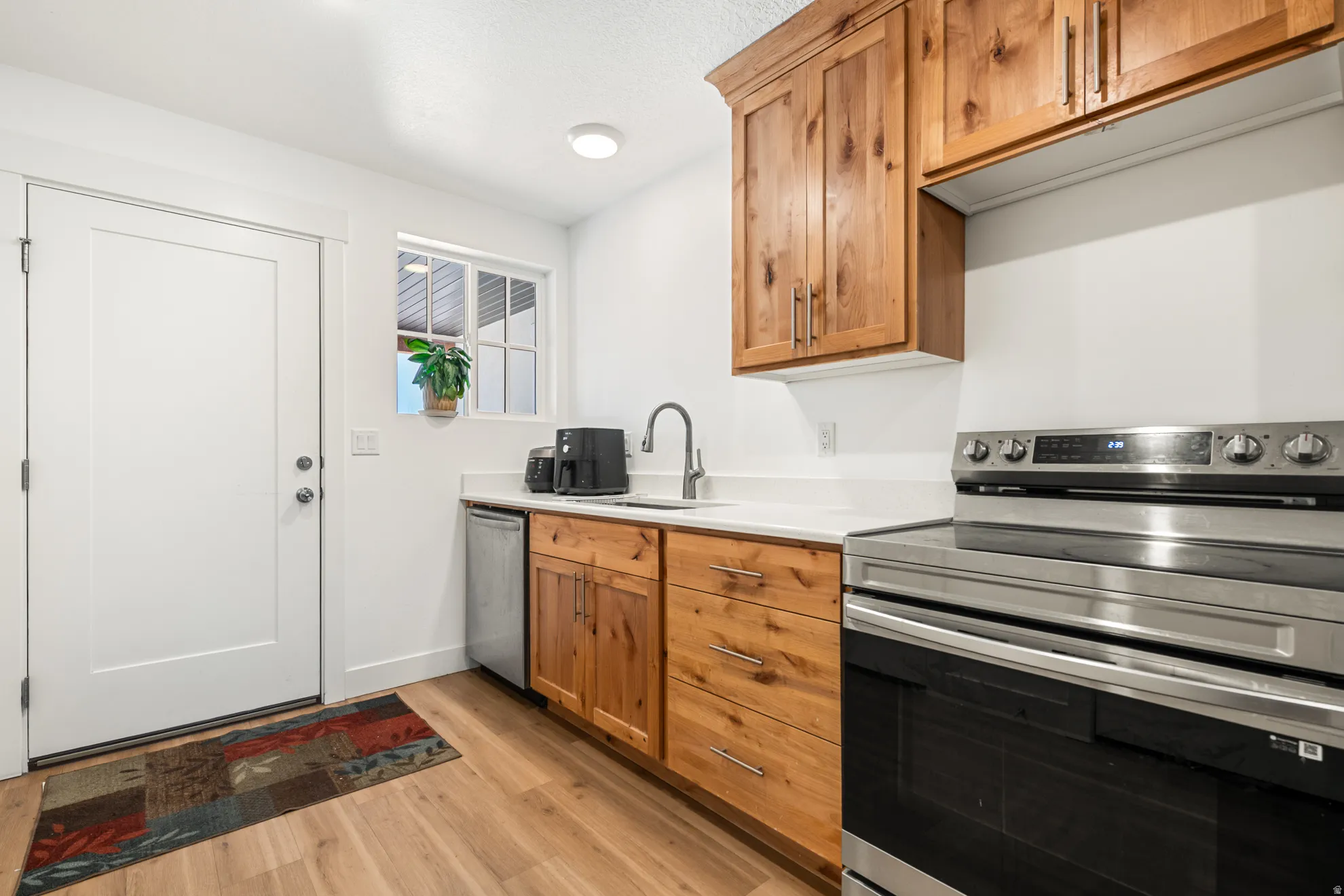 Kitchenette featuring wood-finish cabinetry, stainless steel range, built-in dishwasher, white countertops, and wood-finish flooring