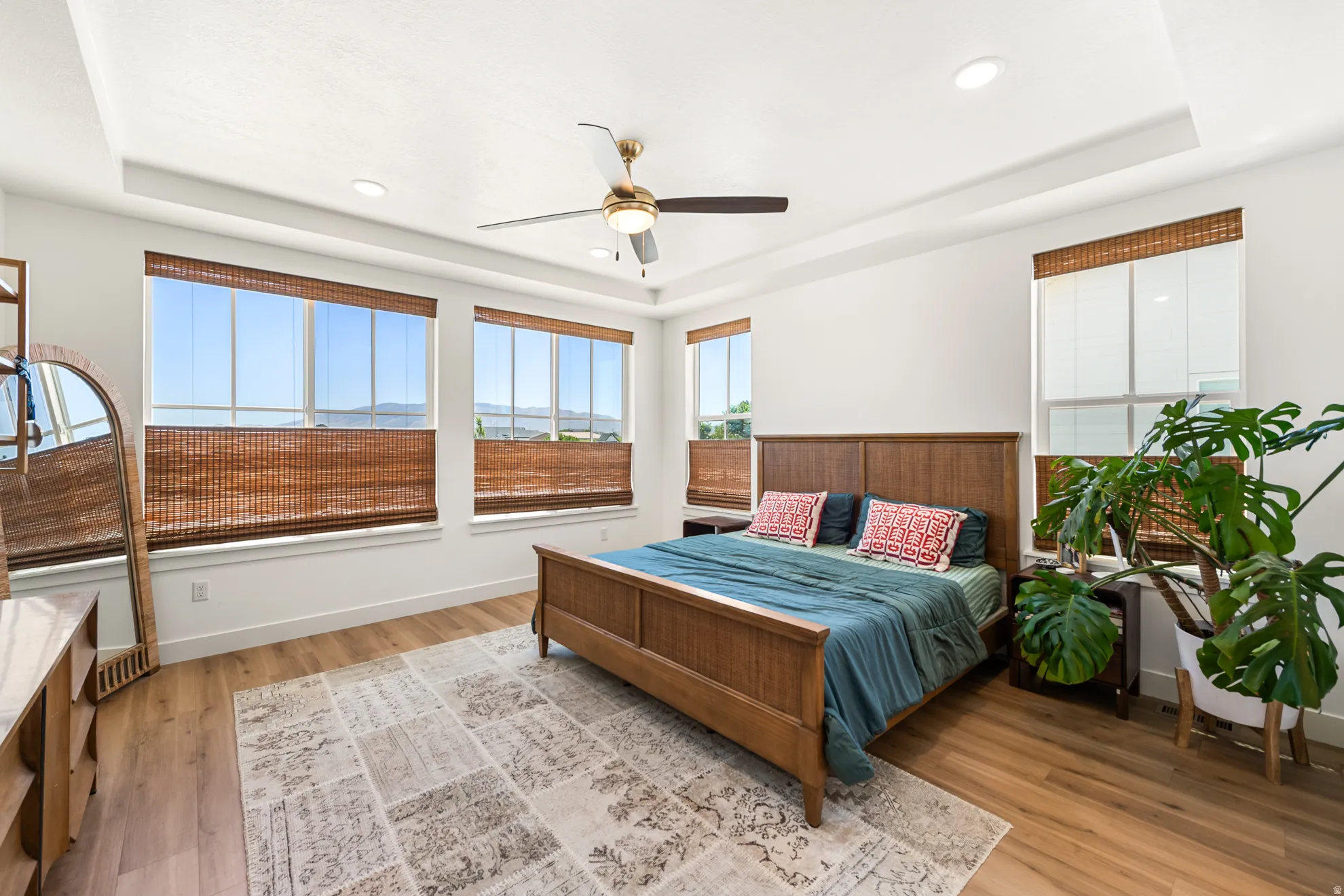 Spacious bedroom featuring light wood-finish flooring and a tray ceiling with recessed lighting