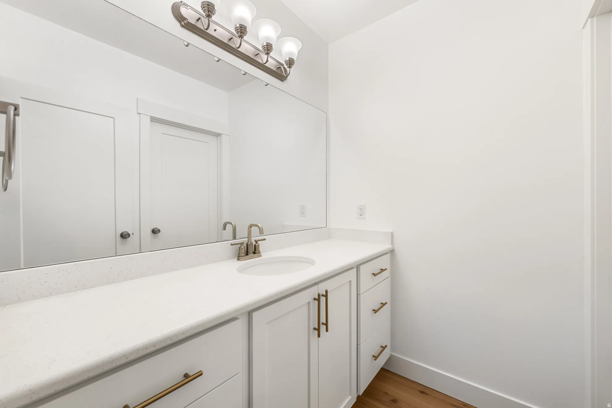 Bathroom vanity featuring a light-toned countertop, white cabinetry with brass hardware, and an undermount sink