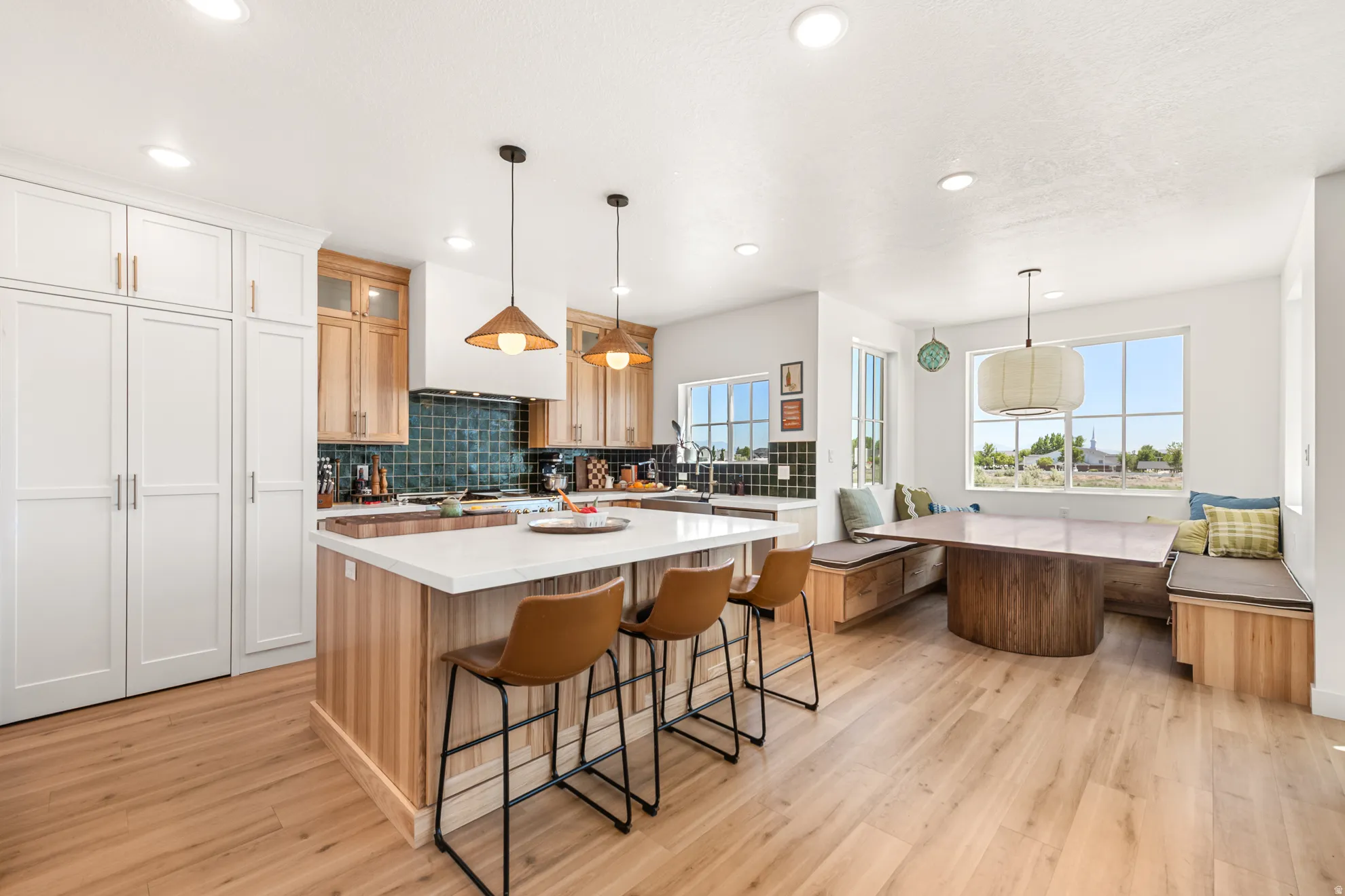 Spacious kitchen featuring an expansive island with white countertop, wood-finish flooring, built-in bench seating with storage, white cabinetry, and natural wood upper cabinets