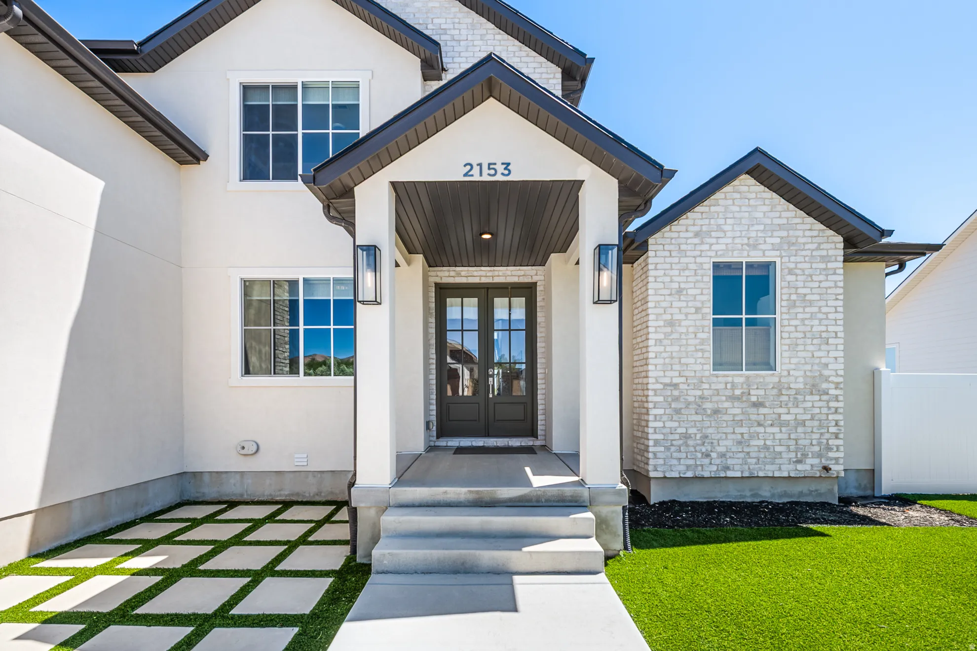 Contemporary two-story exterior featuring a covered entry, dark-frame double entry doors, and a combination of white stucco and light brick siding
