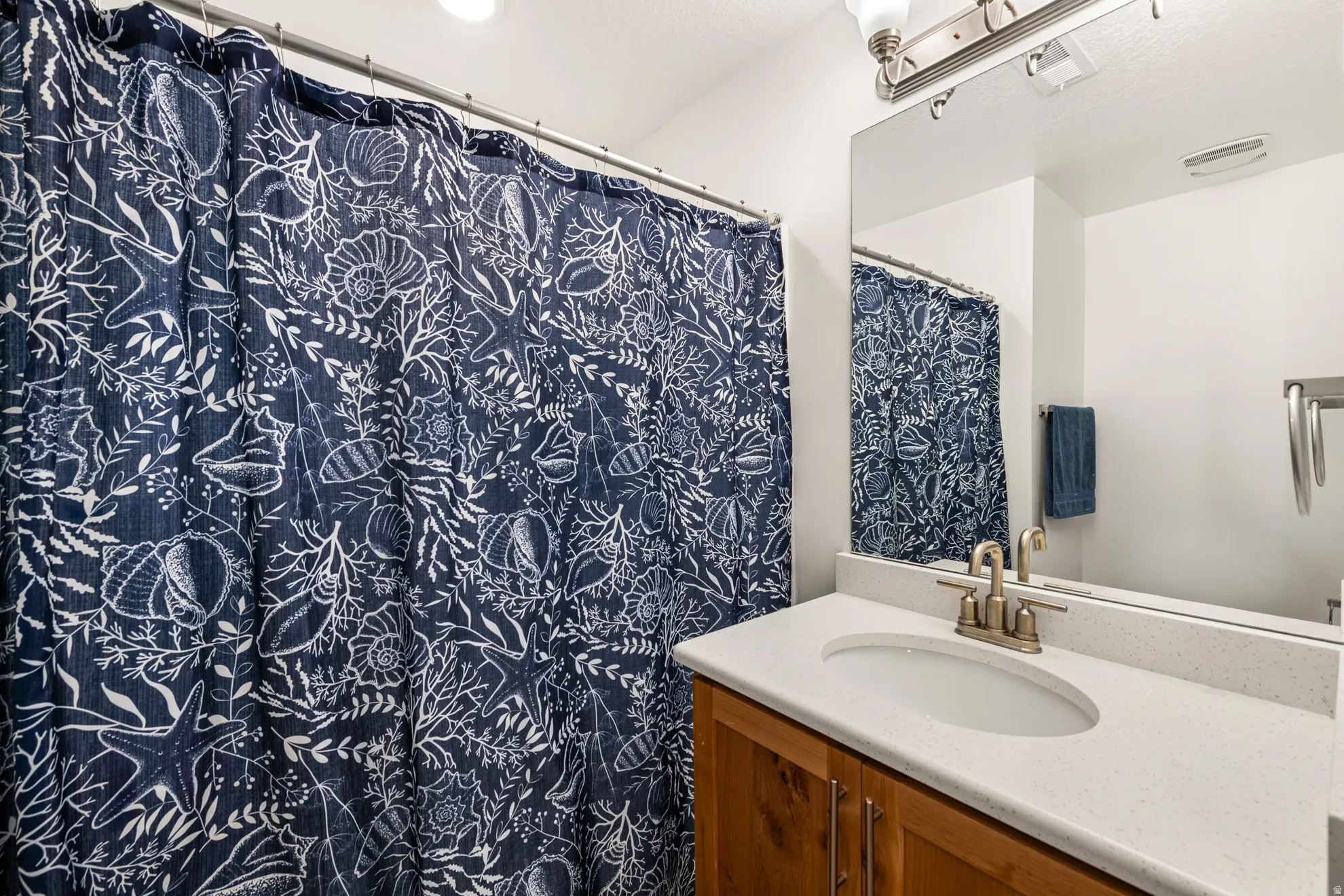 Bathroom featuring a wood-finish vanity with a light countertop, an integrated sink, and an expansive wall mirror