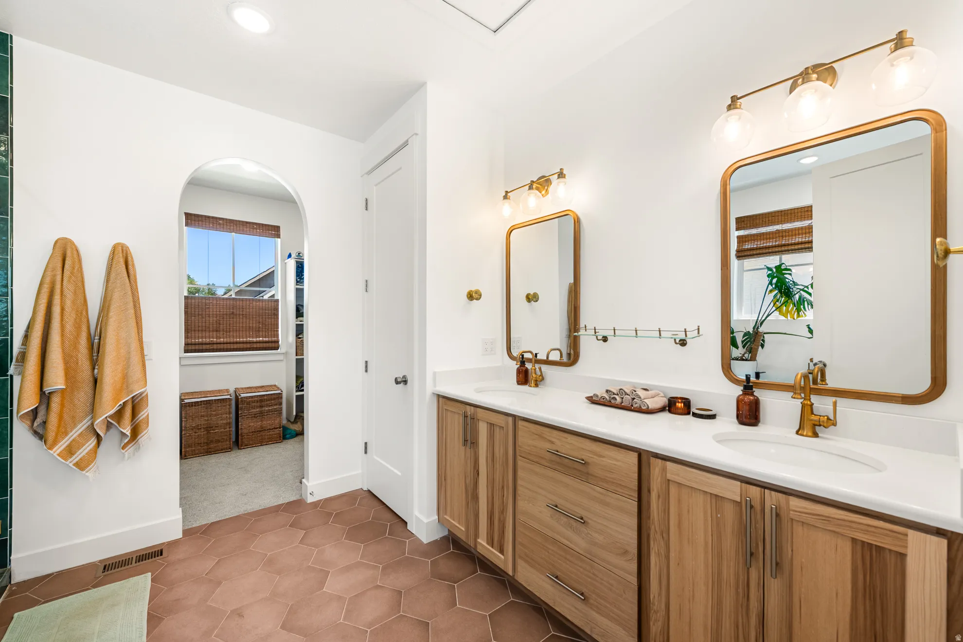 Dual vanity with wood-finish cabinetry, white countertops, and brass hardware