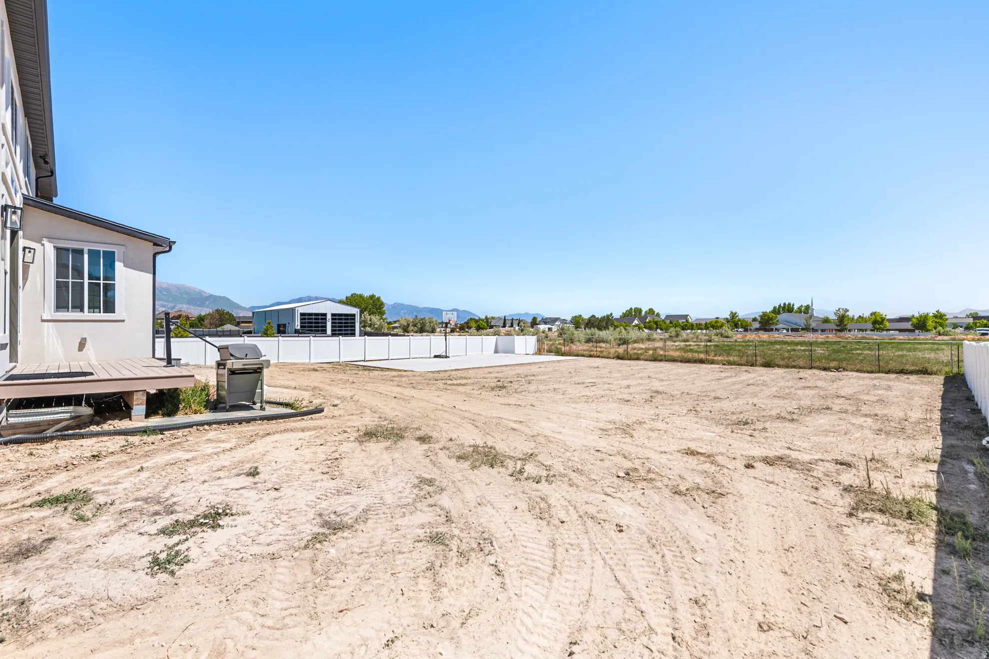 Expansive undeveloped backyard space featuring a composite deck, white vinyl fencing, and a concrete pad