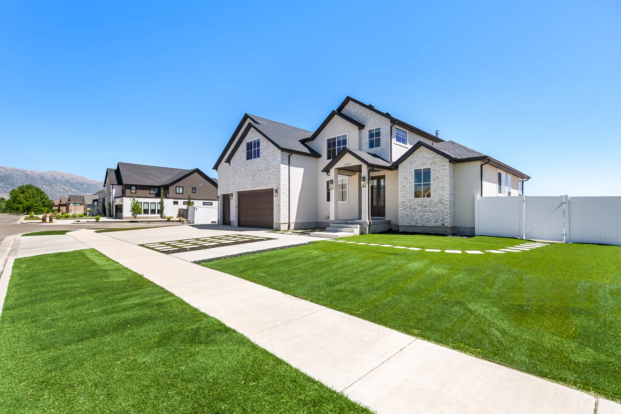 Contemporary home exterior featuring a white brick and stucco facade, dark trim, and a black shingled roof