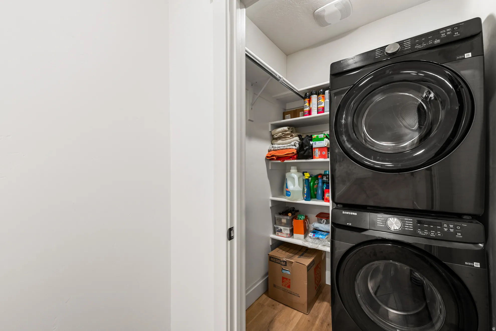 Dedicated laundry closet featuring a stacked washer and dryer, integrated shelving, and wood-finish flooring