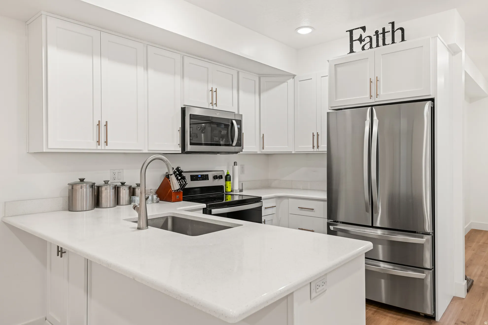 Modern kitchen featuring white cabinetry, light-toned countertops, stainless steel appliances, and wood-finish flooring