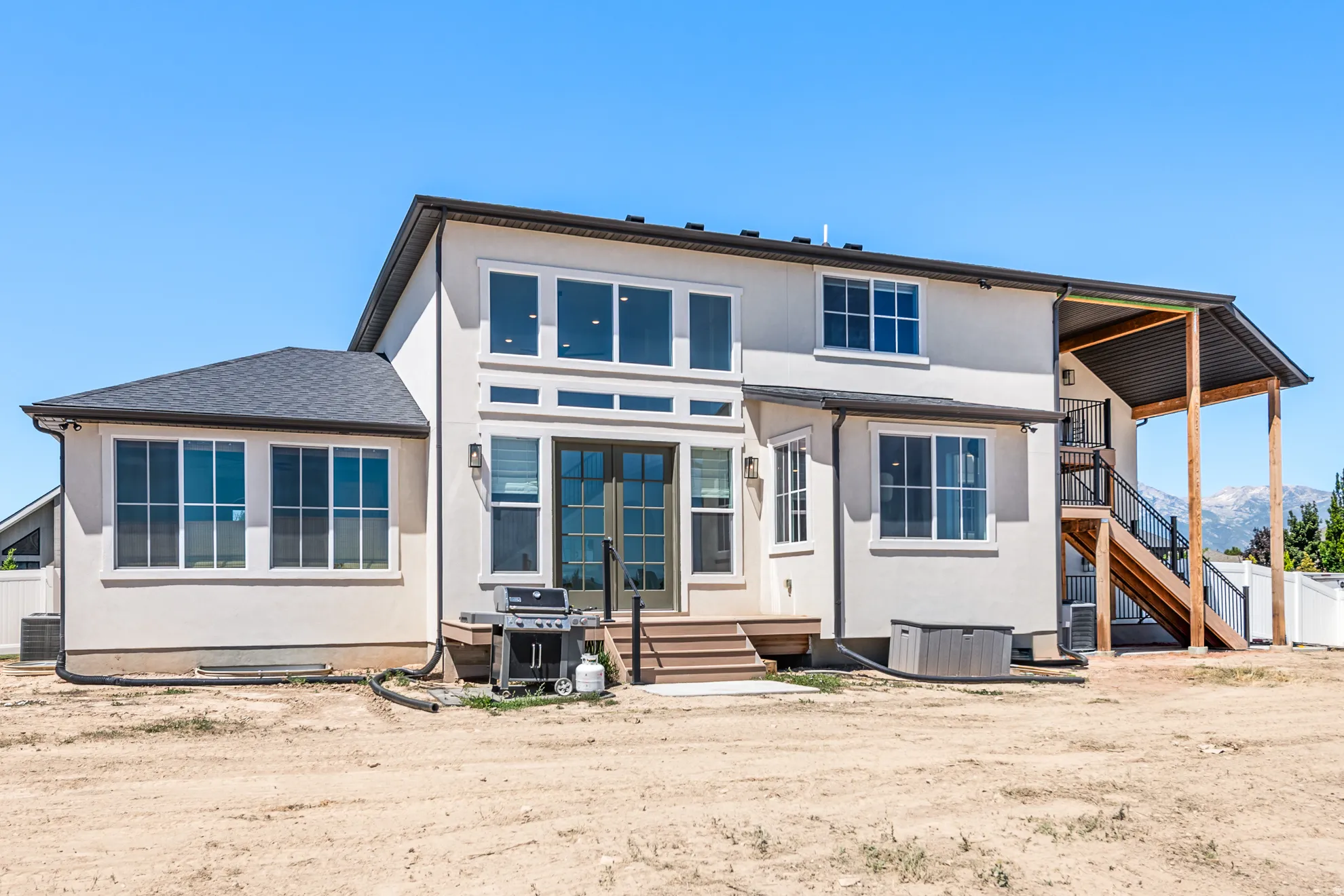 Rear facade featuring multi-level windows, a covered deck with stairs, and a walk-out patio